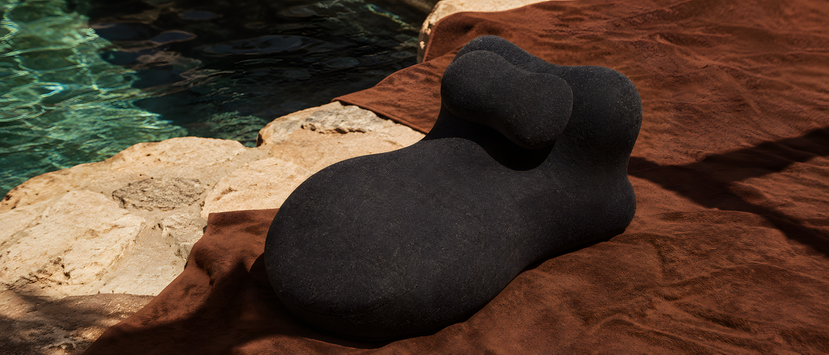 The Amoret pillow on a brown towel at the stone edge of a pool, hard afternoon light